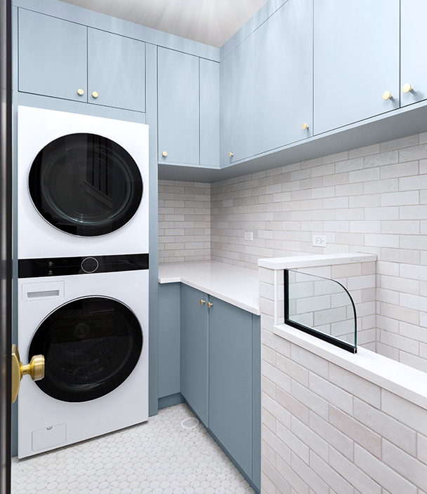 A modern luxurious laundry room with powder blue cabinets with a white washer and dryer